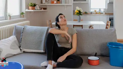 Woman sitting on couch next to buckets for collected water leaking from ceiling.