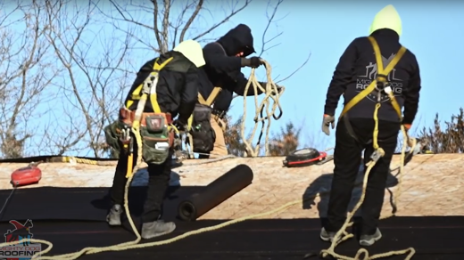 Three people standing on a roof wearing safety equipment